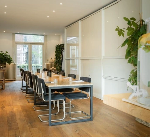 Vergaderruimte aan de Van Baerlestraat met lange tafel, moderne stoelen en veel groen.